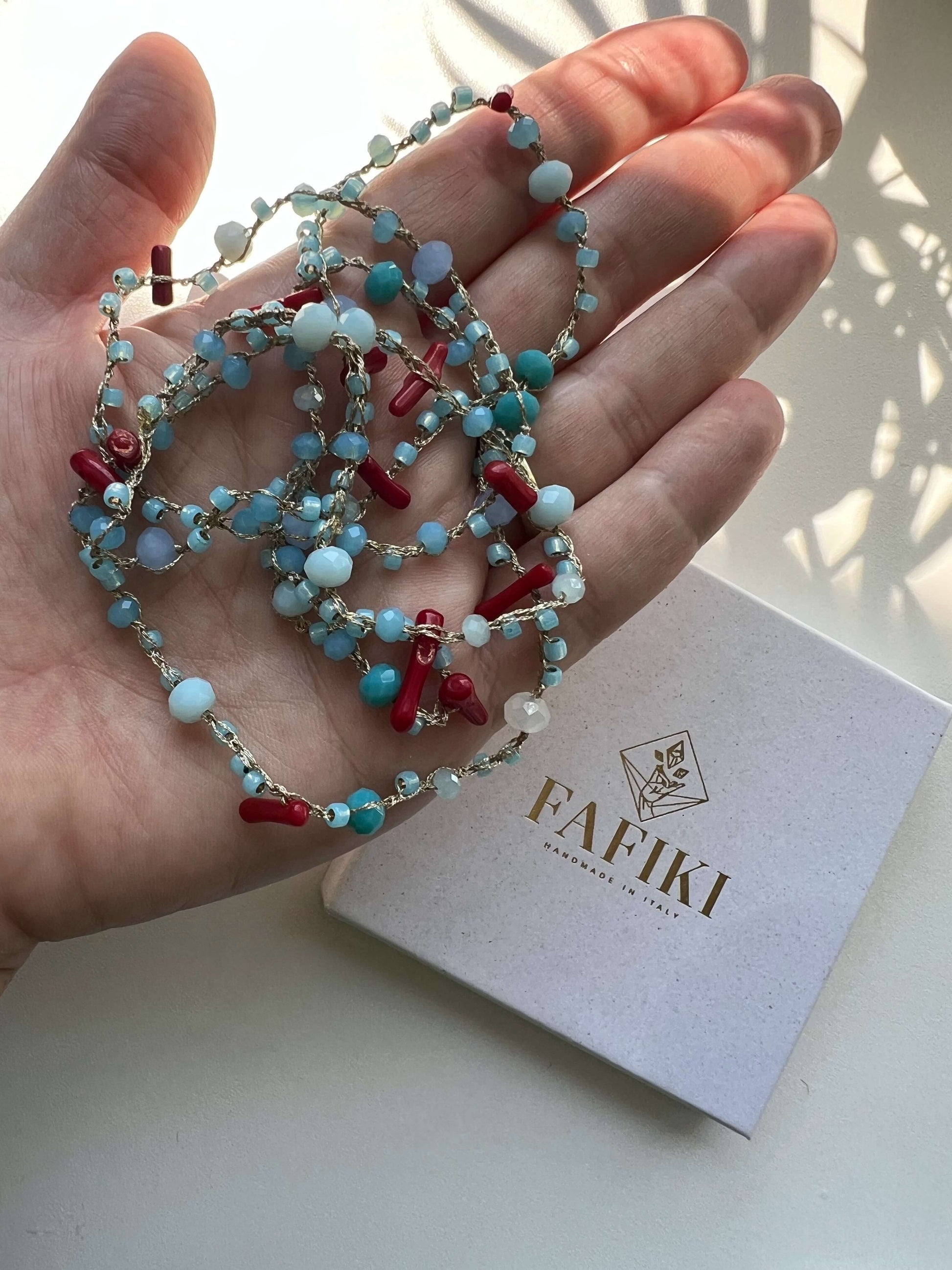 Collana lunga boho in corallo rosso e cristalli azzurri. Realizzata a mano in filato italiano leggero, ipoallergenica e perfetta per pelli sensibili.