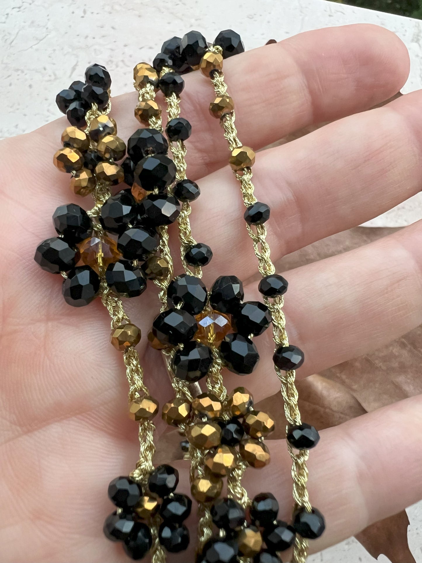 Collana lunga boho chic in oro nero con cristalli e fiori, versatile da indossare come collana o bracciale wrap, perfetta per aggiungere un tocco di eleganza e personalità al tuo look.