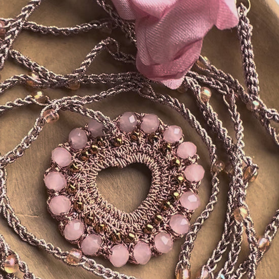Collana lunga cuore rosa cipria con dettagli rame e petali, gioiello boho elegante perfetto per look sofisticati e romantici.