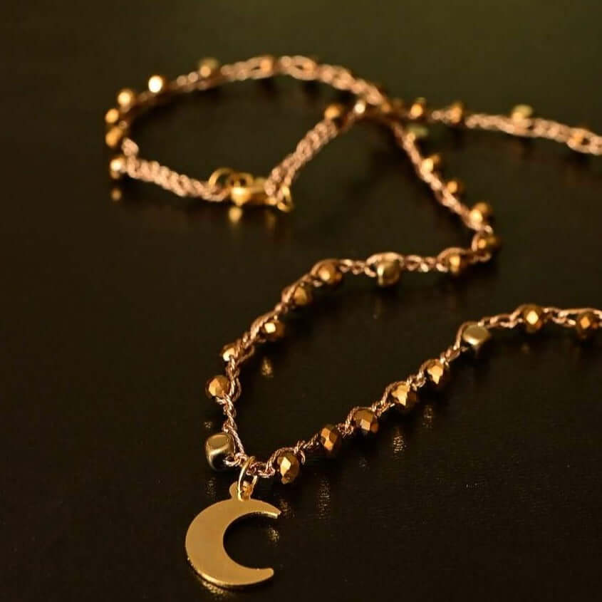 Girocollo artigianale Fafiki in color oro, realizzato con cristalli dorati e pietre di ematite color oro. Caratterizzato da una delicata luna in acciaio inossidabile, questo gioiello lungo 42 cm è dotato di chiusura a moschettone in acciaio galvanizzato. Perfetto per chi cerca un accessorio elegante e versatile, questo girocollo aggiunge un tocco di stile unico a ogni outfit, rendendolo un regalo ideale per le occasioni speciali.