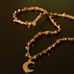 Girocollo artigianale Fafiki in color oro, realizzato con cristalli dorati e pietre di ematite color oro. Caratterizzato da una delicata luna in acciaio inossidabile, questo gioiello lungo 42 cm è dotato di chiusura a moschettone in acciaio galvanizzato. Perfetto per chi cerca un accessorio elegante e versatile, questo girocollo aggiunge un tocco di stile unico a ogni outfit, rendendolo un regalo ideale per le occasioni speciali.
