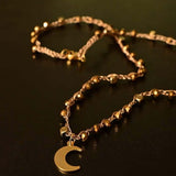 Girocollo artigianale Fafiki in color oro, realizzato con cristalli dorati e pietre di ematite color oro. Caratterizzato da una delicata luna in acciaio inossidabile, questo gioiello lungo 42 cm è dotato di chiusura a moschettone in acciaio galvanizzato. Perfetto per chi cerca un accessorio elegante e versatile, questo girocollo aggiunge un tocco di stile unico a ogni outfit, rendendolo un regalo ideale per le occasioni speciali.