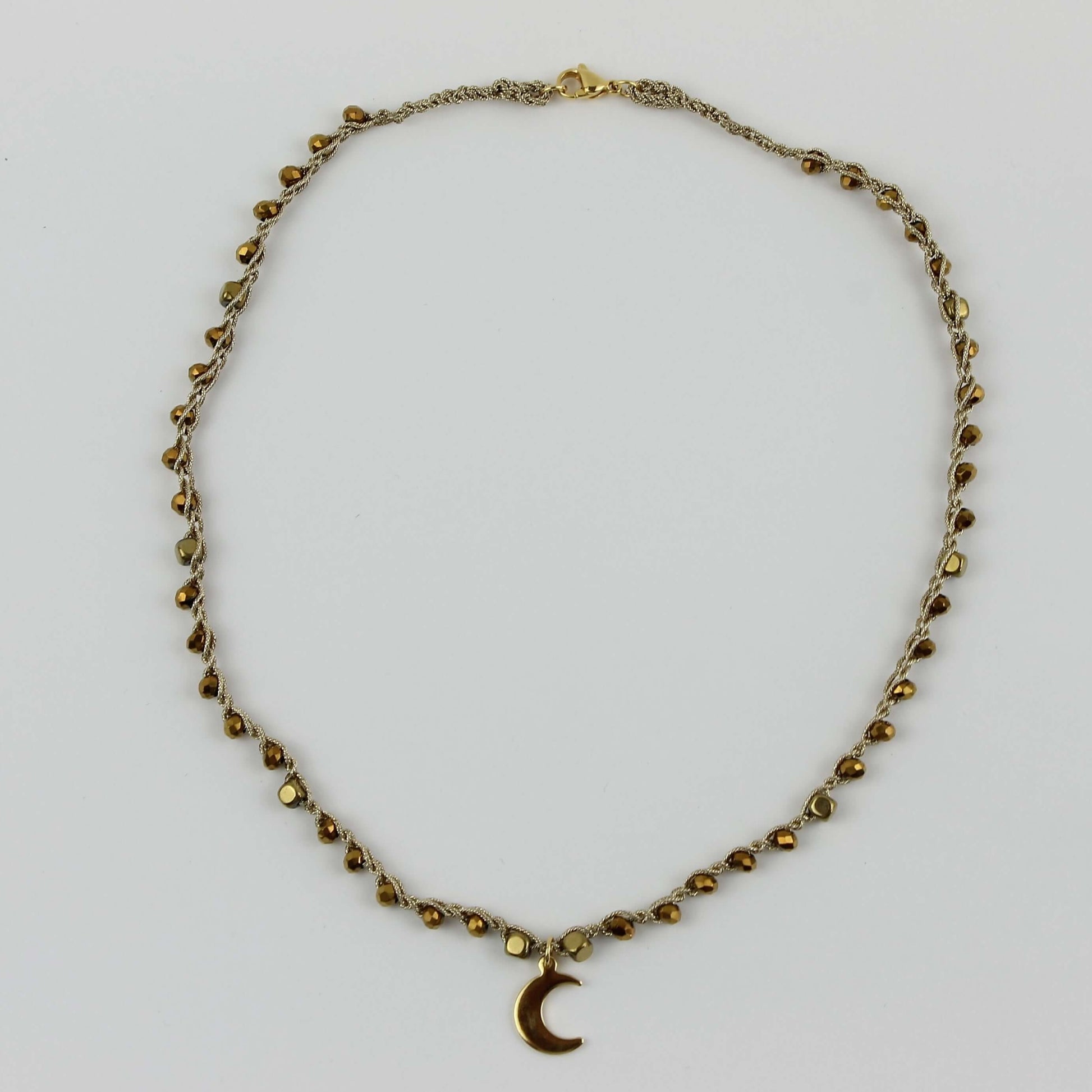 Girocollo artigianale Fafiki in color oro, realizzato con cristalli dorati e pietre di ematite color oro. Caratterizzato da una delicata luna in acciaio inossidabile, questo gioiello lungo 42 cm è dotato di chiusura a moschettone in acciaio galvanizzato. Perfetto per chi cerca un accessorio elegante e versatile, questo girocollo aggiunge un tocco di stile unico a ogni outfit, rendendolo un regalo ideale per le occasioni speciali.