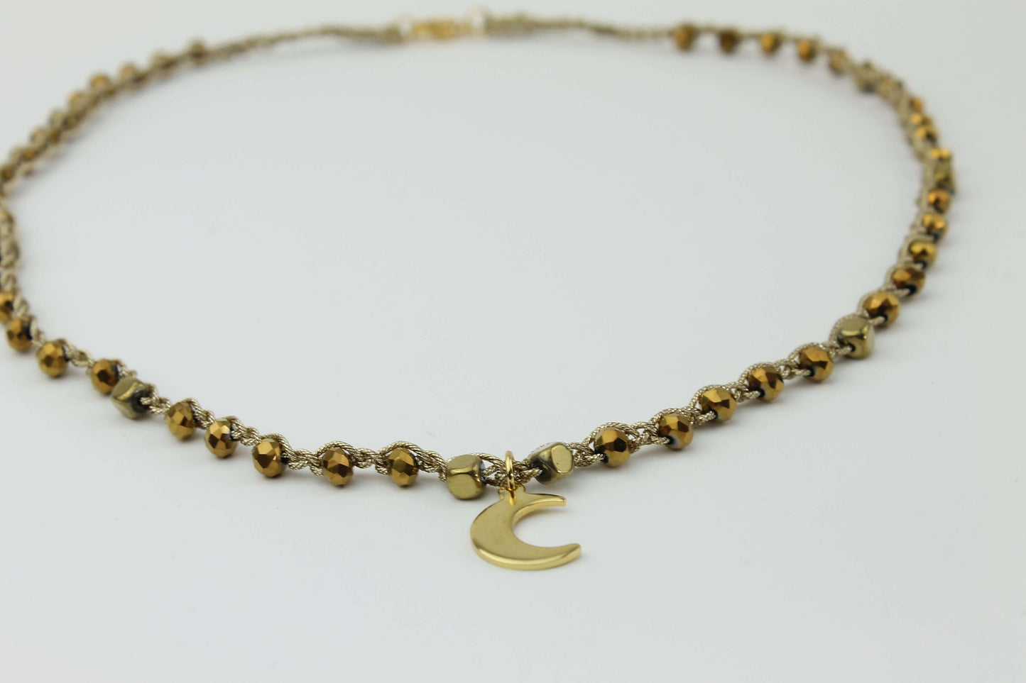 Girocollo artigianale Fafiki in color oro, realizzato con cristalli dorati e pietre di ematite color oro. Caratterizzato da una delicata luna in acciaio inossidabile, questo gioiello lungo 42 cm è dotato di chiusura a moschettone in acciaio galvanizzato. Perfetto per chi cerca un accessorio elegante e versatile, questo girocollo aggiunge un tocco di stile unico a ogni outfit, rendendolo un regalo ideale per le occasioni speciali.