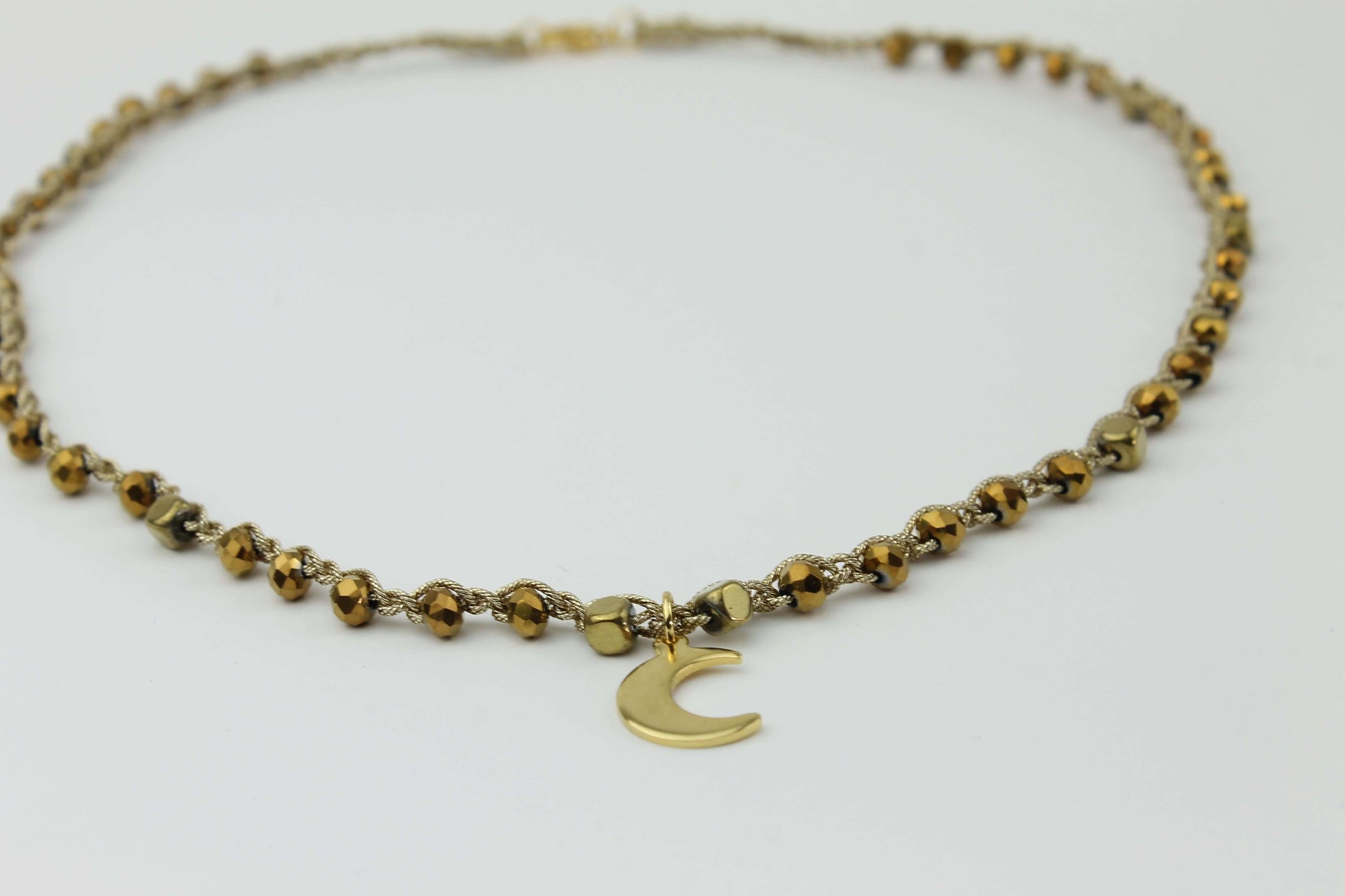 Girocollo artigianale Fafiki in color oro, realizzato con cristalli dorati e pietre di ematite color oro. Caratterizzato da una delicata luna in acciaio inossidabile, questo gioiello lungo 42 cm è dotato di chiusura a moschettone in acciaio galvanizzato. Perfetto per chi cerca un accessorio elegante e versatile, questo girocollo aggiunge un tocco di stile unico a ogni outfit, rendendolo un regalo ideale per le occasioni speciali.