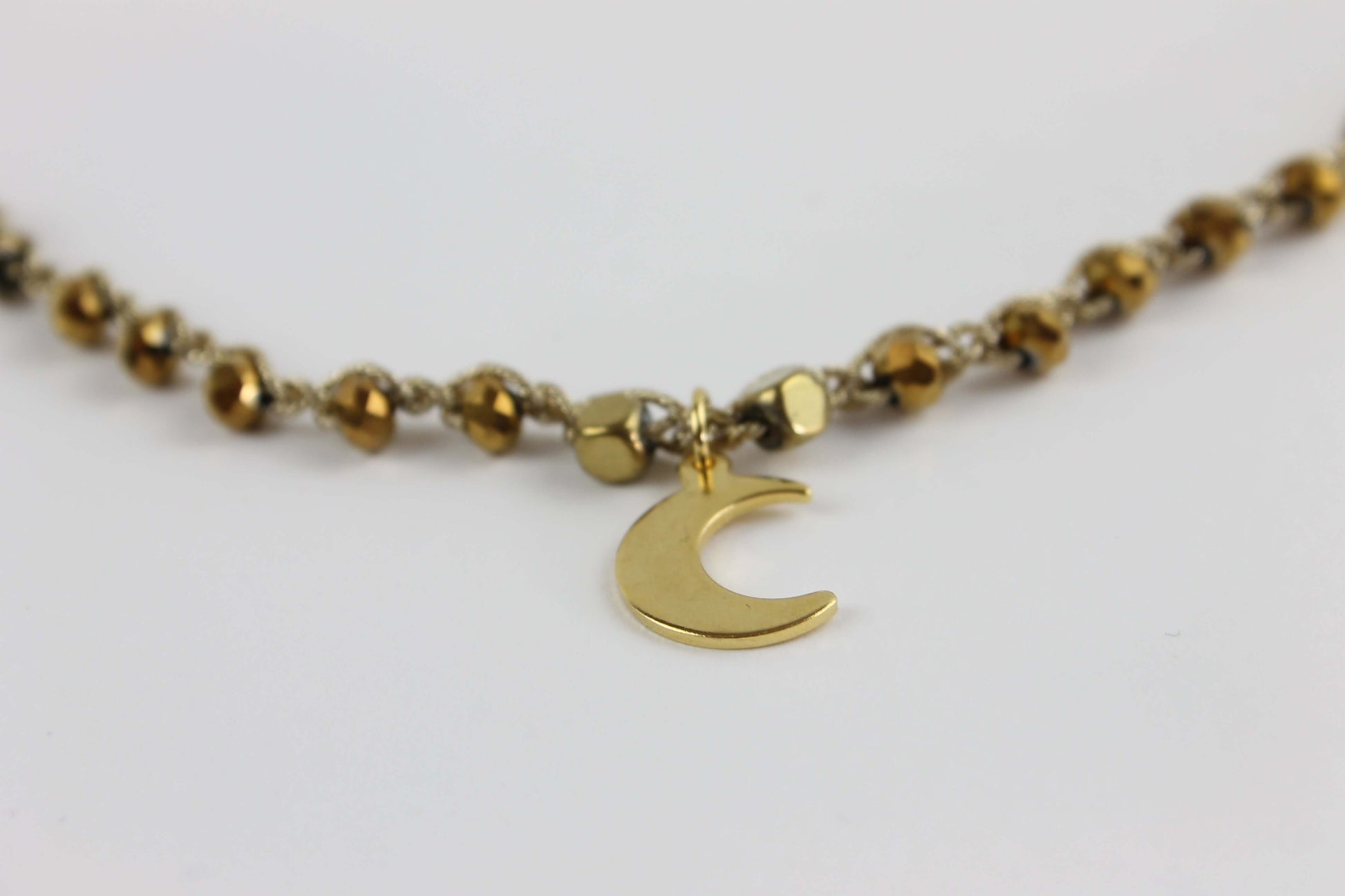 Girocollo artigianale Fafiki in color oro, realizzato con cristalli dorati e pietre di ematite color oro. Caratterizzato da una delicata luna in acciaio inossidabile, questo gioiello lungo 42 cm è dotato di chiusura a moschettone in acciaio galvanizzato. Perfetto per chi cerca un accessorio elegante e versatile, questo girocollo aggiunge un tocco di stile unico a ogni outfit, rendendolo un regalo ideale per le occasioni speciali.